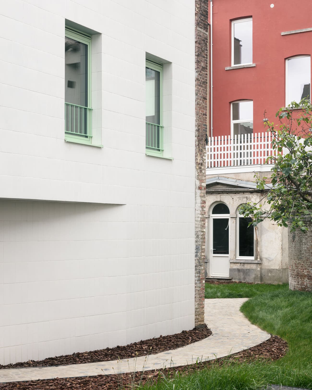 Architectural project - green accents, urban dwelling, contrasting colors, red building, residential exterior, curved path, townhouse design, sleek architecture, tiled facade, light green windows, urban courtyard, paving stones, crisp design, sustainable city, refined aesthetic, minimal design, urban setting, city living, outdoor space, eco design, outdoor area, green, neutral tones, city architecture, compact space, bright colors, geometric design, light tones, modern facade, clean lines, white facade, white, brick, residential architecture, minimalist exterior, modern home, garden path, green lawn, modern living, contemporary vibe, urban garden, architectural contrast, white tiles, tiles, urban exterior, red
