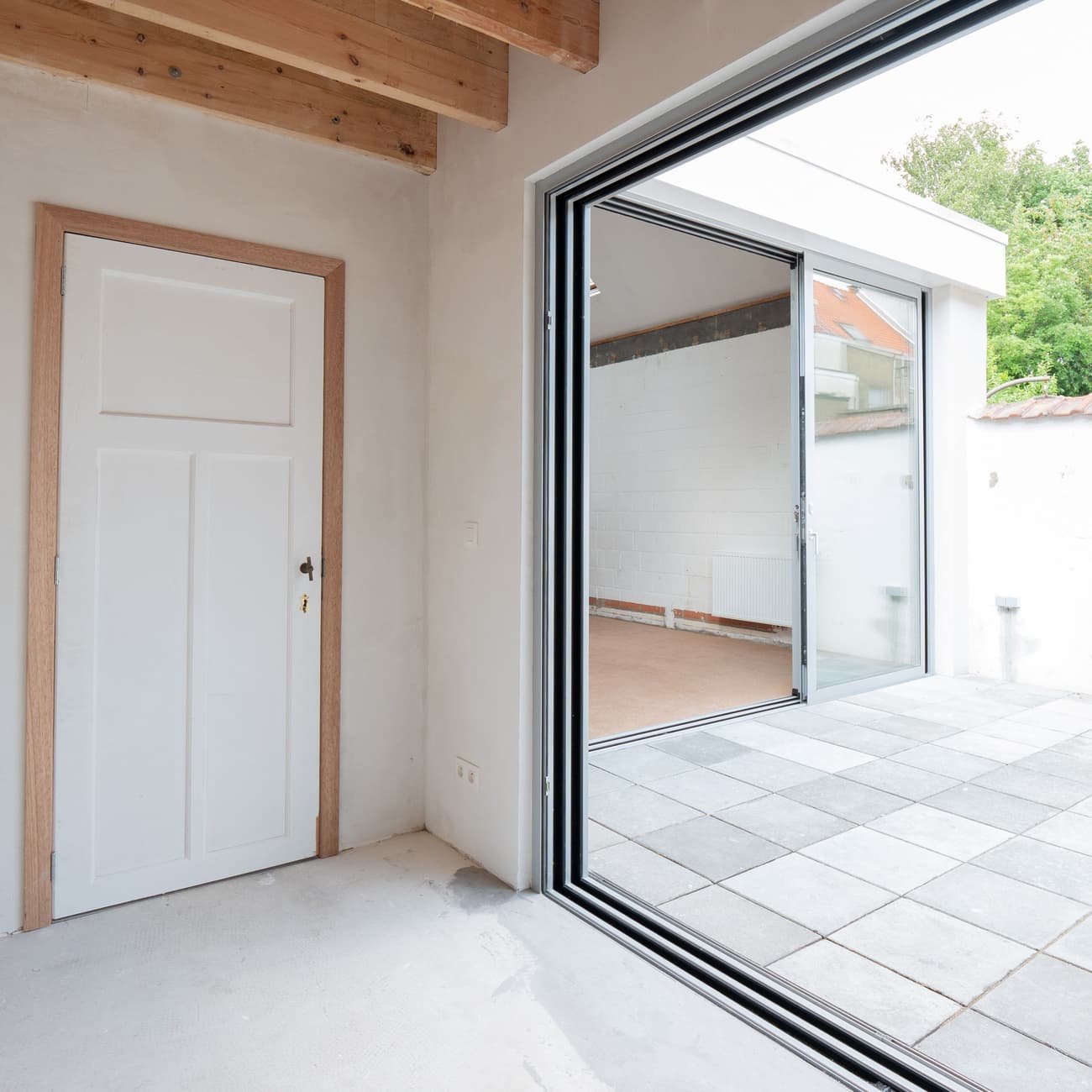 Architectural project - patio space, white door, simple aesthetics, renovation project, sustainable materials, wood, timber, wooden frame, natural light, passive design, glass, contemporary style, exposed beams, daylight, beige, concrete, light wood, modern aesthetic, timber beams, neutral palette, minimalist design, glass doors, warm wood, eco home, clean lines, light filled, indoor outdoor, white, architectural details, large window, plaster wall, energy efficient, stone, plaster, beige tones, open layout, open plan, garden view, minimalist space, stone floor, bright interior, sliding doors, seamless transition, practical design, picture window, spacious feel, multipurpose room, entryway, outdoor terrace