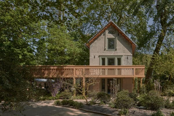 Architectural project - stone facade, terrace, farmhouse touch, natural shade, secluded house, plaster exterior, wraparound deck, treehouse vibe, natural materials, wood, timber, outdoor living, warm tones, neutral tones, daylight, beige, brown, eco friendly, Scandinavian influence, natural setting, sunlight, rustic charm, earth tones, biophilic design, sustainable home, large windows, energy efficient, stone, plaster, rustic style, earthy tones, pitched roof, tree canopy, forest retreat, nature connection, nature retreat, rural setting, garden view, green design, peaceful vibe, cozy exterior, serene landscape, inviting exterior, sliding doors, passive solar, home, timber railing, warm palette, country home