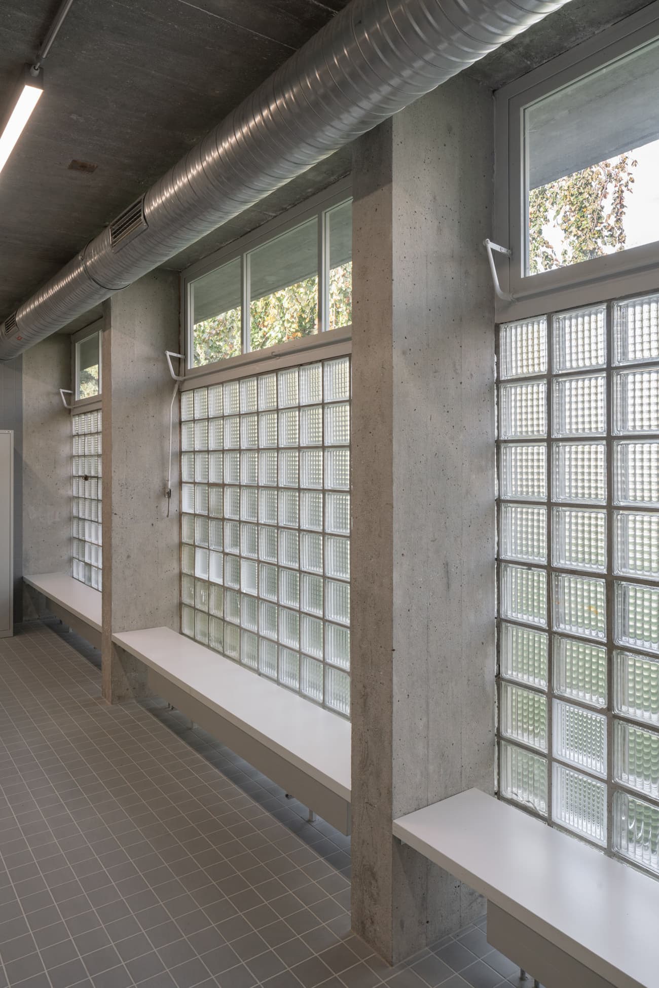 Architectural project - raw concrete, silver, modern industrial, utilitarian style, urban renewal, modern workspace, contemporary office, airy interior, streamlined design, grey tiles, light filled room, concrete walls, glass blocks, linear lighting, structured space, block windows, ductwork ceiling, exposed duct, grid tiles, geometric patterns, indoor environment, eco-friendly design, industrial design, steel, natural light, recycled materials, glass, sustainable architecture, grey, concrete, minimal aesthetics, functional design, neutral palette, passive cooling, adaptive reuse, industrial chic, clean lines, white, architectural details, daylight use, energy efficiency, simple bench, minimalist interior, built-in bench, urban style, modular elements, office space