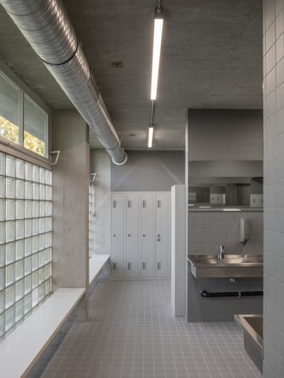 Architectural project - silver, industrial interior, exposed ductwork, commercial space, urban aesthetic, smooth textures, concrete ceiling, concrete walls, steel accents, reflective surfaces, glass bricks, grid pattern, linear lighting, minimalist bathroom, modern fixtures, utilitarian space, public locker room, tiled walls, gray tiles, grey flooring, stainless steel sink, industrial sink, fluorescent lighting, ample storage, locker storage, functional restroom, spatial efficiency, steel, natural light, grey, neutral tones, industrial vibe, concrete, functional design, neutral palette, durable materials, clean lines, light filled, modern architecture, robust design, raw finish, sleek design, airy atmosphere, contemporary space, muted tones, urban style, practical layout