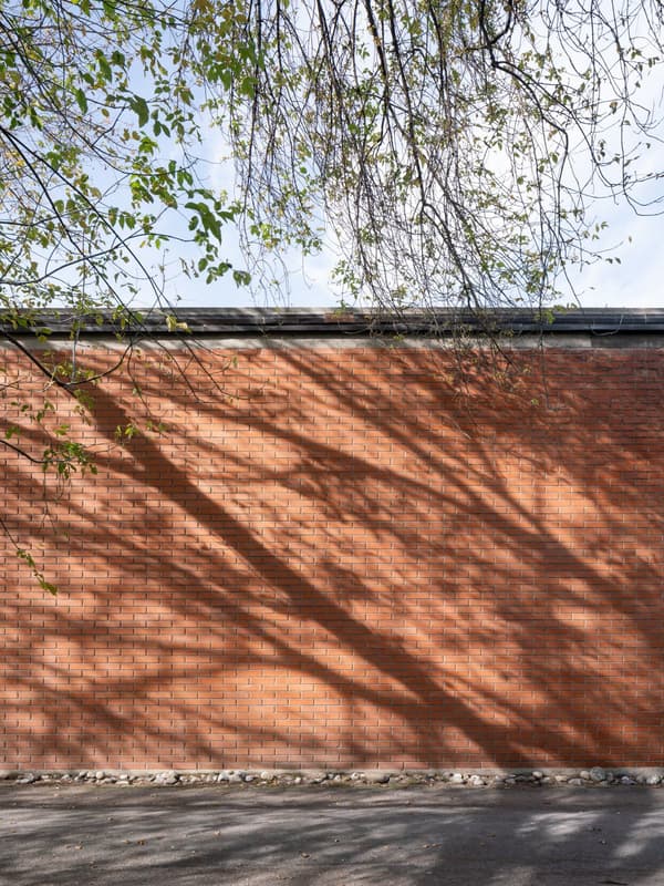 Architectural project - design element, raw aesthetic, brick wall, exposed brick, orange brick, textured brickwork, natural shadows, linear texture, tree shadow, outdoor facade, eco friendly facade, minimalist, urban setting, outdoor space, natural light, shadow play, passive design, sustainable design, warm tones, brown, exterior design, geometric pattern, exterior wall, industrial style, daylight optimization, facade detail, contemporary design, neutral palette, minimalist design, exterior, orange, textured surface, modern facade, architectural simplicity, simple elegance, earthy tones, brick facade, urban architecture, building envelope, sleek finish, structural rhythm, architectural feature, urban backdrop