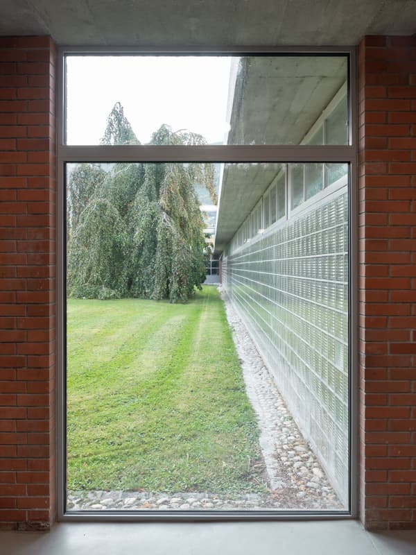 Architectural project - exterior facade, brick wall, landscape, horizontal windows, concrete ceiling, transitional space, glass blocks, lawn, structured space, connection, minimal design, minimalist, architectural detail, industrial design, natural light, sustainable design, glass, warm tones, eco design, grey, green, neutral tones, daylight, industrial vibe, brown, concrete, building facade, industrial style, contemporary, simple design, modern, clean lines, indoor outdoor, large window, glass window, outdoor view, textured wall, framed view, brick, outdoor connection, red brick, garden view, open view, green space, urban style