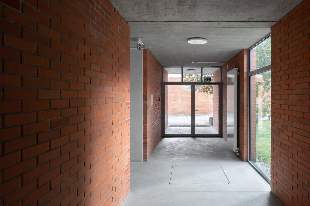 Architectural project - linear design, passageway, concrete ceiling, transitional space, exposed brick, polished concrete, indoor atmosphere, understated style, brick walls, red bricks, symmetry, rectangular space, light fixtures, indoor passage, minimal details, neutral color palette, transition zone, indoor walkway, raw materials, natural light, privacy screen, functional space, daylight, city architecture, industrial style, functional design, contemporary design, minimalist design, glass doors, large windows, modern architecture, open layout, modern hallway, grey floor, sleek design, concrete floor, simple lines, clean design, corridor, hallway, practical design, geometric form, urban vibe, urban interior