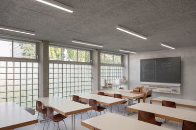 Architectural project - grid windows, minimalist furniture, timber desk, classroom, educational, school room, modern classroom, glass block windows, wood desk, sleek chairs, student chairs, teaching board, chalkboard, blackboard, white desks, brown chairs, study environment, academic setting, low energy, minimalist learning, natural light, passive design, sustainable design, modern vibe, neutral tones, daylight, light wood, functional design, daylight optimization, eco friendly, minimalist vibe, contemporary design, neutral palette, minimalist design, neutral colors, clean lines, large windows, plaster wall, beige tones, open plan, study area, bright interior, simple decor, efficient layout, open space, educational space, learning space, wooden furniture, modern education, learning environment, concrete wall, bright room