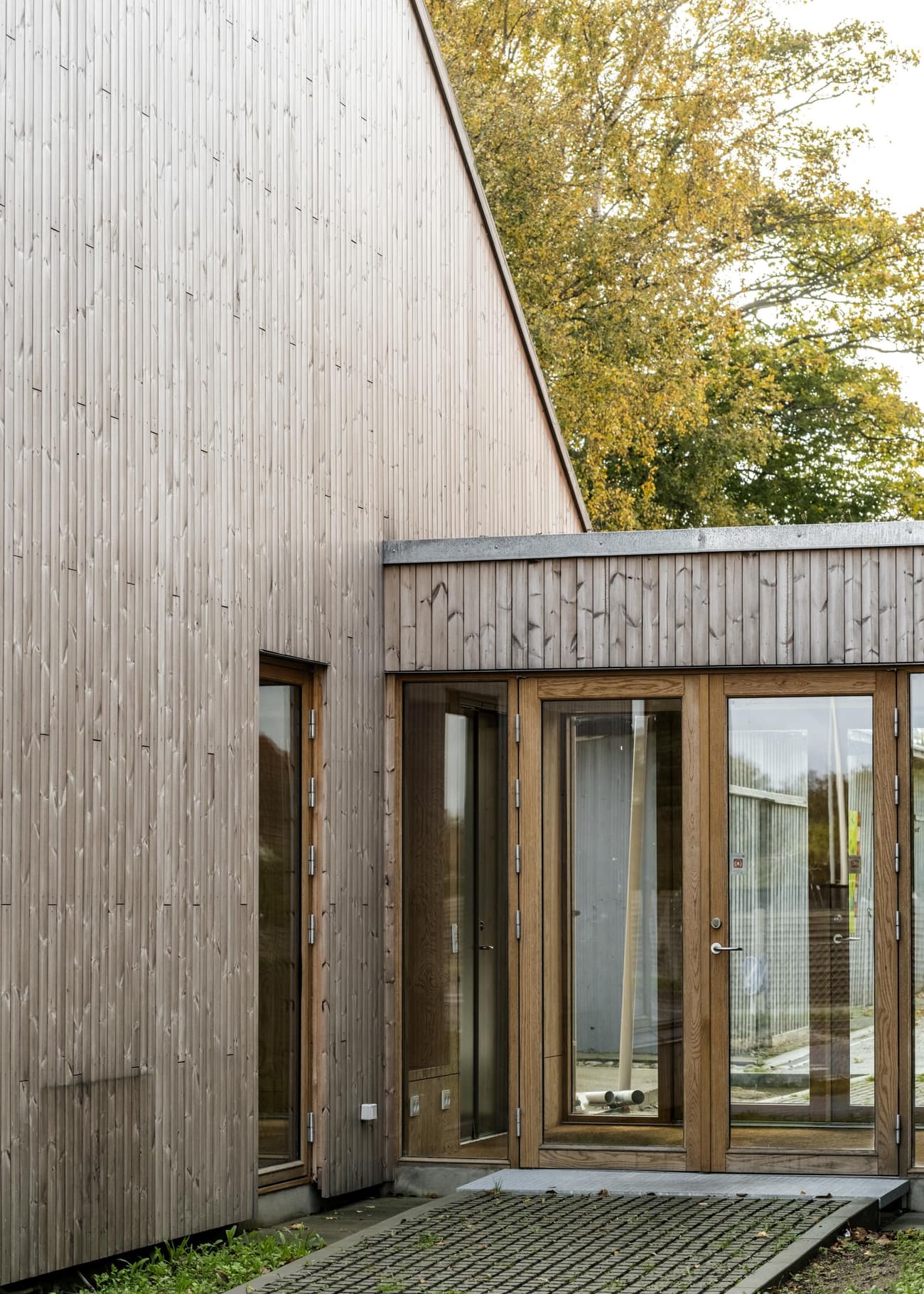 Architectural project - low carbon home, natural materials, wood, timber, outdoor space, natural light, sustainable design, yellow, glass, warm tones, sustainable architecture, grey, green, daylight, beige, brown, timber facade, minimalist facade, eco friendly, timber construction, Scandinavian style, neutral palette, exterior, biophilic design, eco home, passive house, contemporary home, landscape integration, wood cladding, Nordic design, harmonious design, modern architecture, energy efficient, inviting entrance, compact design, wood texture, earthy tones, garden view, eco architecture, residential building, seamless integration, home design, vertical slats, modern exterior, wooden building