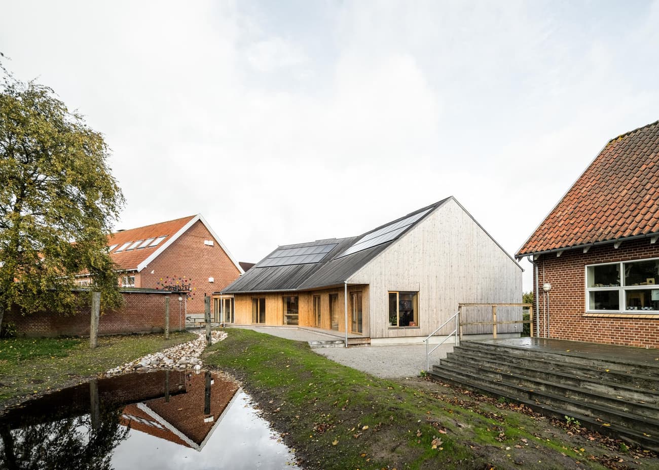 Architectural project - terrace, natural facade, minimal facade, solar panel, garden, solar panels, countryside vibe, modern barn, rustic elements, serene environment, wood, timber, outdoor space, warm tones, sustainable architecture, neutral tones, landscape architecture, light wood, eco friendly, rural architecture, low carbon, biophilic design, open landscape, rural design, timber cladding, wood cladding, wood house, timber house, rural home, countryside home, energy efficient, sloped roof, pitched roof, brick, barn style, nature integration, green design, minimalist exterior, water feature, passive solar, modern rural, sustainable living, rural retreat