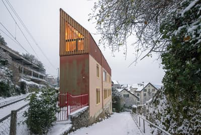 Architectural project - beige facade, urban residential, warm glow, red accent, insulated walls, colorful facade, countryside feel, rustic elements, hillside home, pastel pink, pastel tones, pink, wood, timber, natural light, sustainable design, warm tones, neutral tones, beige, concrete, wood facade, timber facade, eco friendly, rustic charm, minimalist design, eco materials, modern rustic, natural ventilation, scenic view, energy efficient, plaster, cozy exterior, residential home, passive solar, family house, urban architecture, architectural contrast, small windows, red