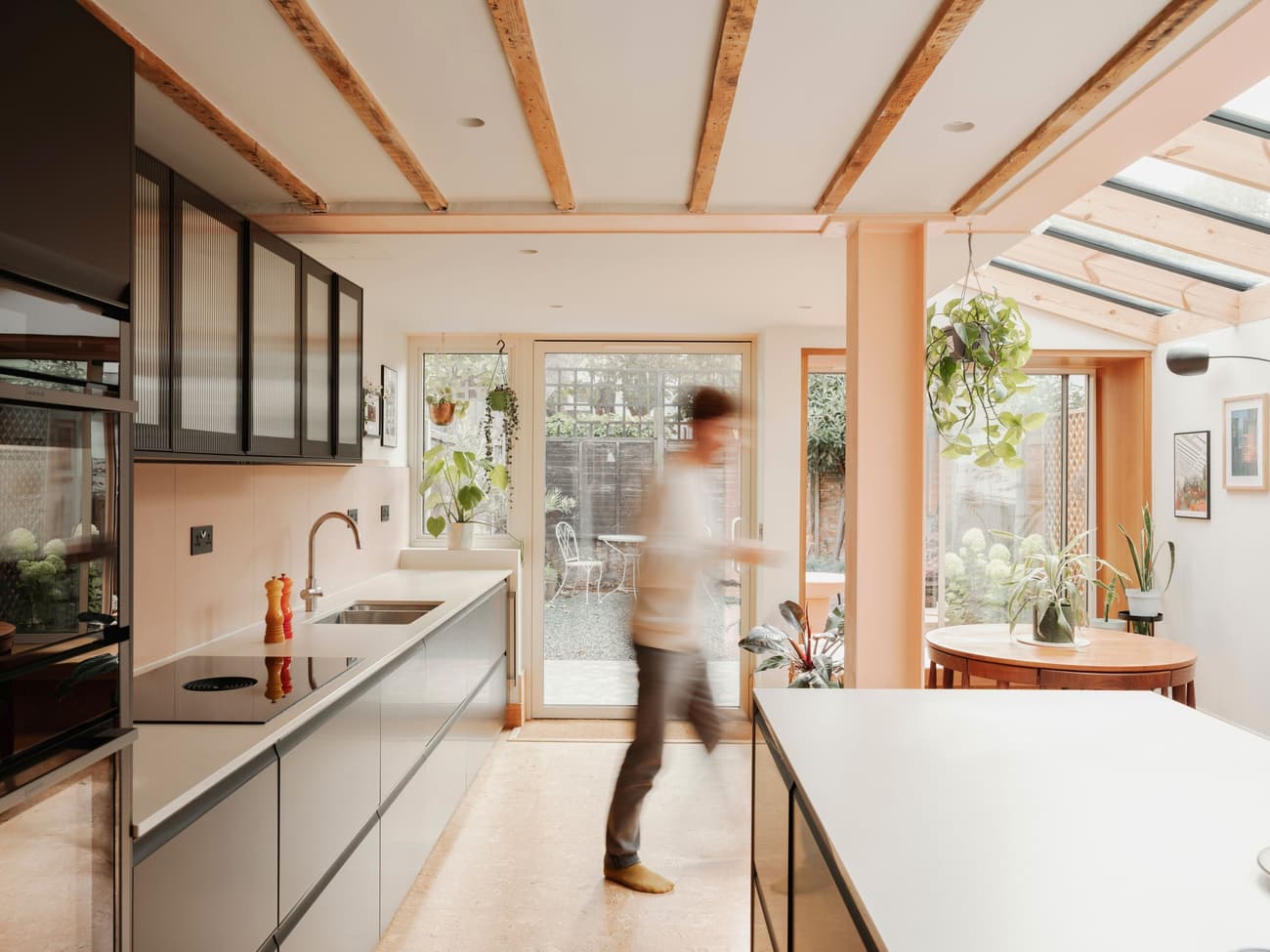 Architectural project - breakfast bar, contemporary kitchen, residential kitchen, reflective surfaces, modern garden, stylish kitchen, sleek cabinetry, black cabinets, warm interior, timber, natural light, sustainable design, glass, warm tones, contemporary style, daylight, beige, light wood, eco friendly, timber beams, neutral palette, minimalist design, black, social space, glass doors, playful elements, biophilic design, sustainable home, indoor outdoor, white, plaster, family kitchen, open layout, open plan, inviting space, casual dining, cozy atmosphere, greenery, garden view, warm vibe, modern kitchen, kitchen island, sliding doors, plaster walls, smooth surfaces, modern interior, skylight, indoor plants