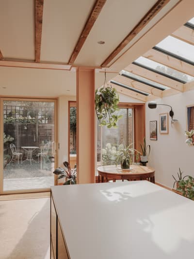 Architectural project - indoor garden, glass roof, plant decor, sunlit space, dining nook, peach walls, hanging plants, warm interior, natural materials, pastel tones, timber, relaxed vibe, natural light, sustainable design, glass, warm tones, green, daylight, beige, light wood, timber beams, minimalist style, relaxed atmosphere, soft textures, modern rustic, biophilic design, eco home, eco friendly home, wood frame, open layout, open plan, inviting space, casual dining, residential design, cozy corner, garden view, earthy palette, comfortable living, interior space, skylight, home renovation, indoor outdoor flow, bright home