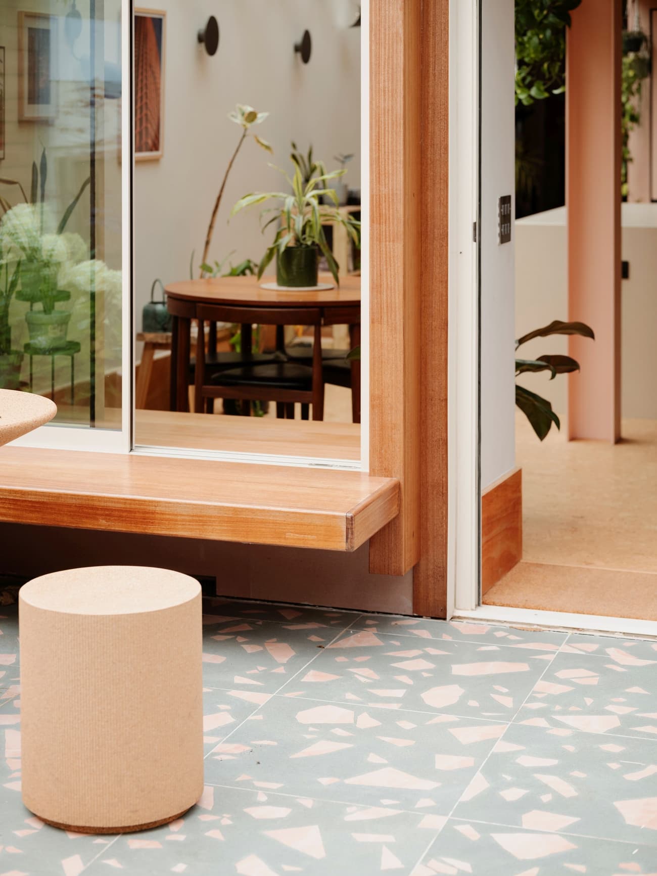 Architectural project - home decor, stylish design, natural elements, house plants, sliding glass, calm environment, inviting area, terrazzo floor, pink wall, wooden bench, sustainable materials, pastel tones, pink, wood, relaxed vibe, natural light, glass, contemporary style, daylight, brown, light wood, eco friendly, neutral palette, timber bench, casual seating, tranquil setting, warm wood, indoor outdoor, cozy nook, earthy tones, warm atmosphere, residential design, greenery, minimalist aesthetic, glass door, comfortable living, open space, minimal decor, soft pink, soft colors, modern interior, indoor plants, versatile space