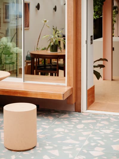 Architectural project - home decor, stylish design, natural elements, house plants, sliding glass, calm environment, inviting area, terrazzo floor, pink wall, wooden bench, sustainable materials, pastel tones, pink, wood, relaxed vibe, natural light, glass, contemporary style, daylight, brown, light wood, eco friendly, neutral palette, timber bench, casual seating, tranquil setting, warm wood, indoor outdoor, cozy nook, earthy tones, warm atmosphere, residential design, greenery, minimalist aesthetic, glass door, comfortable living, open space, minimal decor, soft pink, soft colors, modern interior, indoor plants, versatile space