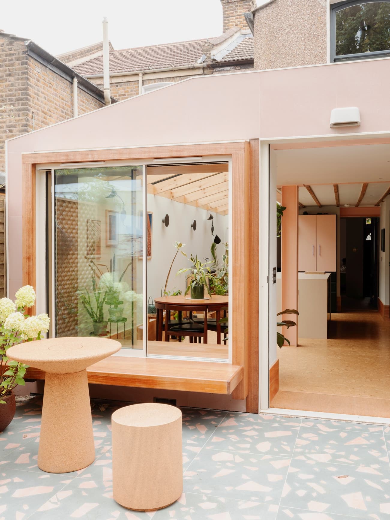 Architectural project - terrace, brick wall, dining room, exposed brick, home extension, modern extension, fresh vibe, patio doors, terrazzo floor, garden room, pastel pink, natural materials, pink, timber, timber frame, relaxed vibe, natural light, sustainable design, warm tones, contemporary architecture, daylight, plywood, beige, light wood, eco friendly, wood beams, timber beams, Scandinavian style, minimalist design, glass doors, indoor outdoor, modern architecture, wood frame, open layout, open plan, dining area, inviting space, cozy atmosphere, residential design, greenery, Nordic influences, family home, bright space, sliding doors, soft colors, courtyard, renovation, indoor plants