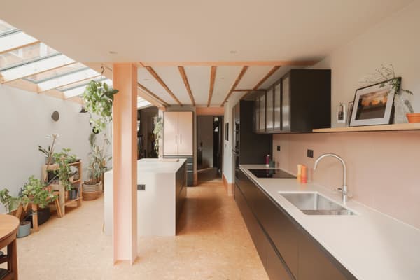 Architectural project - breakfast bar, indoor garden, integrated appliances, cork, open kitchen, black cabinets, white sink, sustainable materials, pink, wood, timber, natural light, glass, warm tones, neutral tones, daylight, beige, sunlight, timber beams, contemporary design, minimalist style, calming space, black, neutral colors, vibrant space, biophilic design, eco friendly home, inviting home, cozy kitchen, family kitchen, home kitchen, warm atmosphere, residential design, bright interior, modern kitchen, sleek design, kitchen island, wood ceiling, sustainable living, open shelving, skylight, airy kitchen, indoor plants