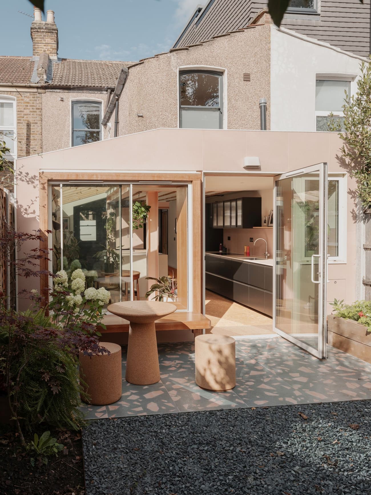 Architectural project - urban greenery, home extension, patio view, modern extension, open doors, garden furniture, backyard, small garden, cozy garden, sleek kitchen, geometric patterns, cork, pastel pink, sustainable materials, wood, city living, playful design, natural light, shadow play, sustainable design, glass, neutral tones, daylight, multifunctional space, eco friendly, flat roof, compact space, Scandinavian style, exterior, outdoor seating, glass doors, geometric design, low carbon, contemporary home, indoor outdoor, cozy vibe, Nordic style, earthy materials, stone, plaster, inviting space, warm atmosphere, greenery, gravel path, modern kitchen, compact living, sliding doors, garden path, urban home