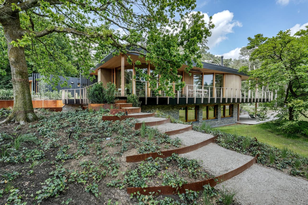 Architectural project - rustic elegance, landscaping, raised platform, airy vibe, elevated home, garden steps, terrace dining, natural architecture, vacation retreat, woodland home, panoramic views, minimalist, eco-friendly design, wood, timber, steel, natural light, glass, warm tones, contemporary style, green, neutral tones, beige, brown, timber facade, wood exterior, outdoor seating, biophilic design, sustainable home, passive house, hillside house, large windows, energy efficient, stone, open plan, forest setting, greenery, nature integration, countryside retreat, gravel path, family home, glass wall, modern cabin
