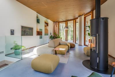 Architectural project - green accents, floor to ceiling windows, living room, wood details, curved ceiling, glass railing, cozy lounge, soft seating, light hardwood, beige furniture, rounded furniture, comfy sofas, black stove, stylish home, wood, timber, natural light, sustainable design, pastel colors, glass, warm tones, contemporary style, green, timber structure, beige, light wood, daylight optimization, eco friendly, Scandinavian style, neutral palette, black, pastel green, biophilic design, clean lines, white walls, large windows, Nordic design, timber ceiling, open layout, minimalist decor, nature-inspired, relaxing space, forest view, modern fireplace, bright interior, calm atmosphere, wood ceiling, family room, wood paneling, modern interior, glass wall, home retreat, indoor plants, urban retreat