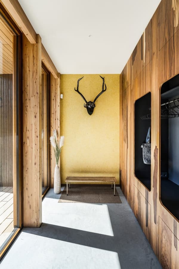 Architectural project - modern entrance, wall niche, welcoming entrance, wooden wall, inviting entry, warm entry, yellow accent, antler decor, unique art, mudroom, small bench, entry seating, chic decor, bright hallway, natural materials, wood, timber, natural light, yellow, glass, warm tones, eco design, grey, neutral tones, concrete, light wood, sunlight, contemporary design, Scandinavian style, minimalist style, cozy space, raw wood, modern rustic, biophilic design, sustainable home, indoor outdoor, cozy vibe, Nordic style, large window, textured wall, energy efficient, minimalist decor, earthy tones, nature-inspired, grey floor, glass door, concrete floor, timber wall, hallway, wood paneling, built-in storage, modern cabin, entryway