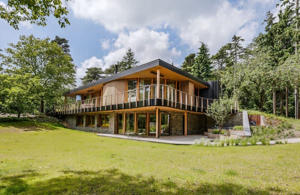 Architectural project - garden patio, stone accents, seamless exterior, hillside home, wraparound balcony, cantilevered design, panoramic windows, daylight home, residential dwelling, idyllic home, natural materials, wood, timber, rustic touch, glass, warm tones, natural tones, eco design, contemporary style, green, beige, timber facade, light wood, eco friendly, wood exterior, natural setting, honey wood, glass doors, tranquil setting, biophilic design, large windows, energy efficient, stone base, stone, sloped roof, forest retreat, forest view, peaceful retreat, landscape design, residential architecture, nature integration, outdoor deck, passive solar, open view, nature blend, green roof, sustainable living, modern cabin, modern retreat, modern house