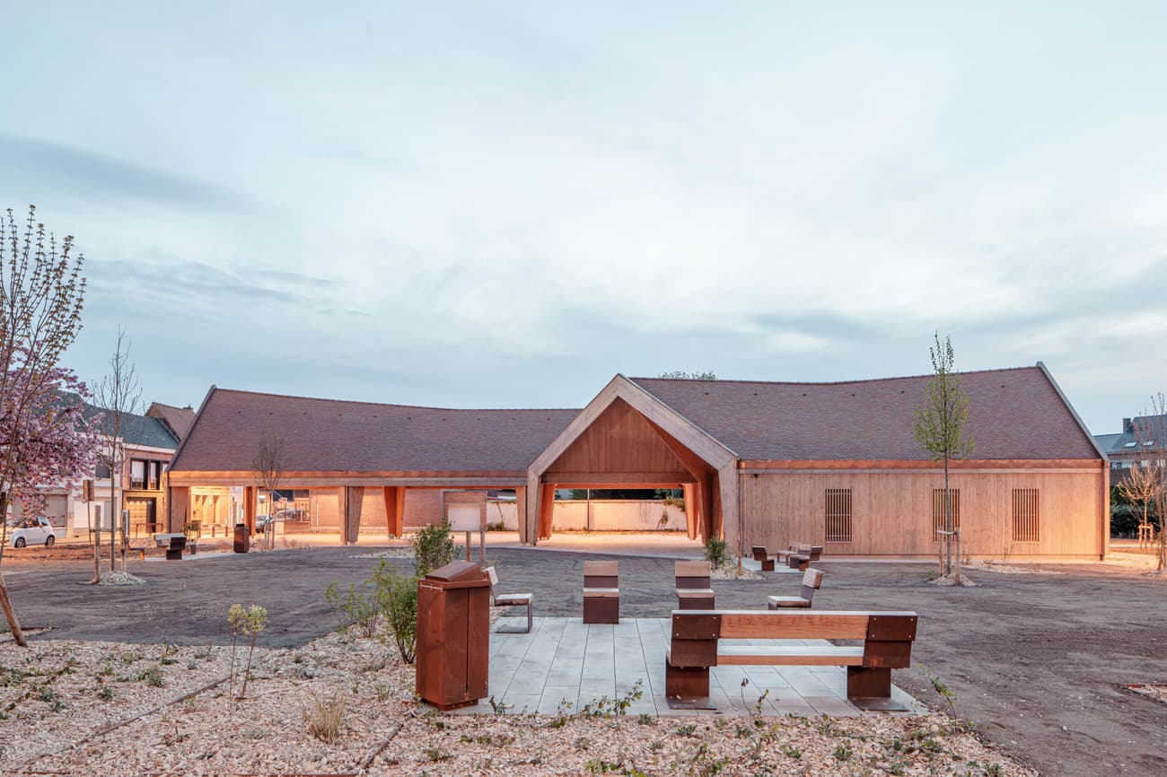 Architectural project - public venue, community gathering, wood furniture, architectural landmark, public seating, outdoor plaza, warm hues, natural materials, sustainable materials, wood, timber, natural light, sustainable design, contemporary style, neutral tones, beige, wood facade, timber facade, low carbon design, eco friendly, timber construction, rustic modern, natural textures, light brown, minimalist design, social space, community hub, gathering area, community center, outdoor seating, landscape integration, clean lines, modern architecture, inviting space, sloped roof, eco architecture, gabled roof, open space, airy atmosphere, wooden exterior, public building, warm lighting