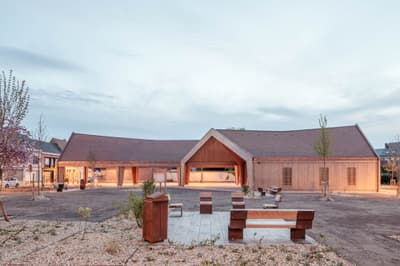 Architectural project - public venue, community gathering, wood furniture, architectural landmark, public seating, outdoor plaza, warm hues, natural materials, sustainable materials, wood, timber, natural light, sustainable design, contemporary style, neutral tones, beige, wood facade, timber facade, low carbon design, eco friendly, timber construction, rustic modern, natural textures, light brown, minimalist design, social space, community hub, gathering area, community center, outdoor seating, landscape integration, clean lines, modern architecture, inviting space, sloped roof, eco architecture, gabled roof, open space, airy atmosphere, wooden exterior, public building, warm lighting