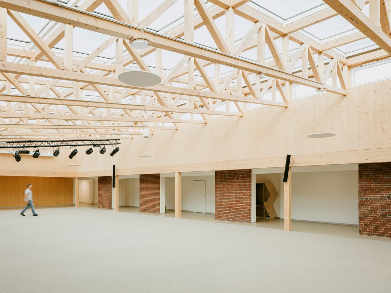 Architectural project - flexible space, passive lighting, brick wall, skylights, welcoming atmosphere, large space, multifunctional hall, acoustic panels, warm interior, eco-friendly design, sustainable materials, wood, timber, natural light, glass, warm tones, green building, contemporary style, neutral tones, daylight, gathering space, beige, brown, exposed trusses, timber trusses, light wood, natural wood, modern design, honey wood, neutral palette, community center, Nordic design, timber ceiling, open plan, inviting space, brick, brick facade, spacious interior, Scandinavian design, bright interior, wood ceiling, public building