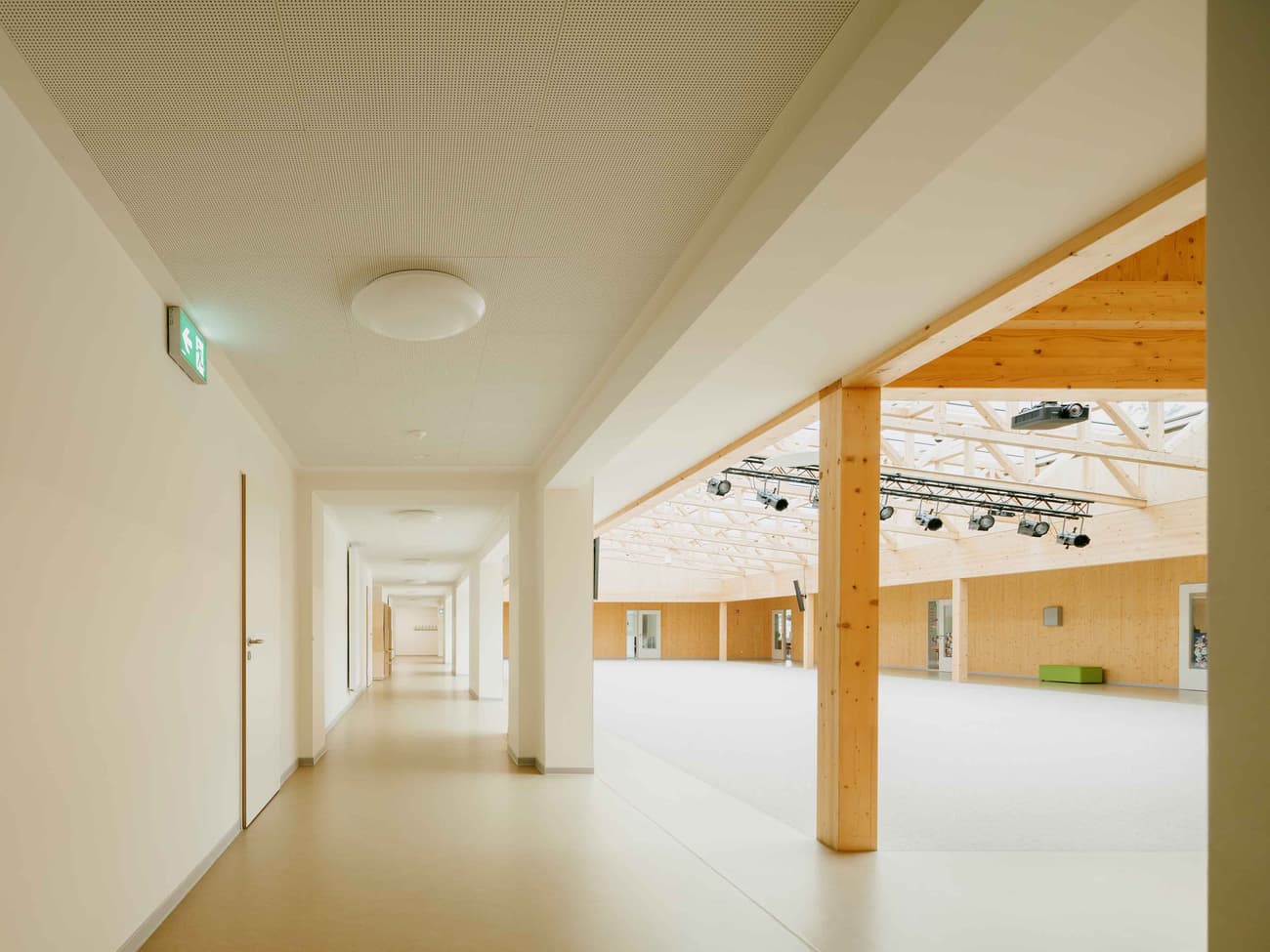 Architectural project - open ceiling, public venue, open span, ceiling lights, modern corridor, bright hallway, minimal design, cozy interior, warm interior, natural materials, soft lighting, wood, timber, raw materials, sustainable design, warm tones, eco design, contemporary architecture, neutral tones, timber structure, exposed beams, daylight, gathering space, beige, brown, light wood, natural wood, golden, wooden beams, sunlight, simple design, honey wood, neutral palette, social space, public space, event space, timber walls, timber cladding, wood cladding, Nordic design, wood walls, timber interior, inviting space, Scandinavian design, bright space, corridor, structural rhythm, wood interior