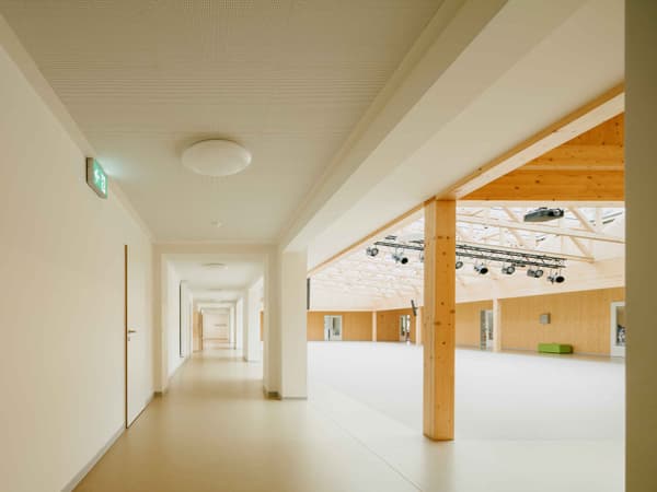 Architectural project - open ceiling, public venue, open span, ceiling lights, modern corridor, bright hallway, minimal design, cozy interior, warm interior, natural materials, soft lighting, wood, timber, raw materials, sustainable design, warm tones, eco design, contemporary architecture, neutral tones, timber structure, exposed beams, daylight, gathering space, beige, brown, light wood, natural wood, golden, wooden beams, sunlight, simple design, honey wood, neutral palette, social space, public space, event space, timber walls, timber cladding, wood cladding, Nordic design, wood walls, timber interior, inviting space, Scandinavian design, bright space, corridor, structural rhythm, wood interior