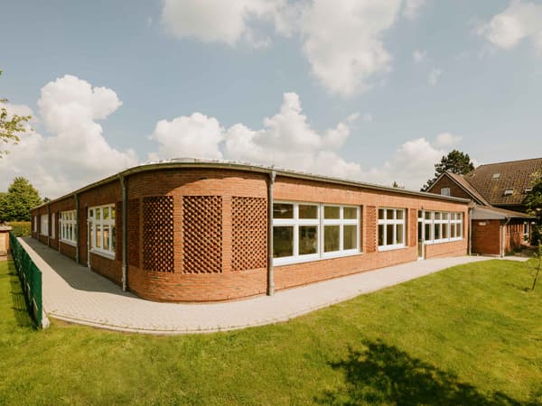 Architectural project - accessible design, brick exterior, educational facility, simple geometry, brick detail, curved facade, single story, eco-friendly design, timber, metal, outdoor space, inviting atmosphere, sustainable design, community space, contemporary architecture, green, neutral tones, brown, functional design, daylight optimization, modular building, durable materials, natural ventilation, large windows, white, landscape design, brick facade, red brick, green lawn, learning space, school building, educational building, modern school, clean design, expansive windows, family-friendly, red, practical layout