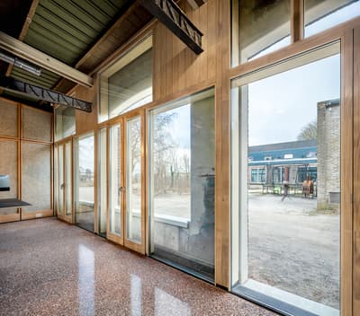 Architectural project - raw finishes, industrial office, modern workspace, commercial building, speckled floor, terrazzo floor, natural materials, wood, timber, steel, natural light, glass, warm tones, sustainable architecture, grey, neutral tones, steel beams, exposed beams, daylight, industrial vibe, brown, light wood, functional design, honey wood, contemporary design, Scandinavian style, neutral palette, timber walls, low carbon, clean lines, large windows, indoor outdoor connection, energy efficient, airy space, exterior view, eco-friendly building, bright interior, floor to ceiling glass, nordic influence, open view, glass facade, wood paneling, minimalist interior, office space