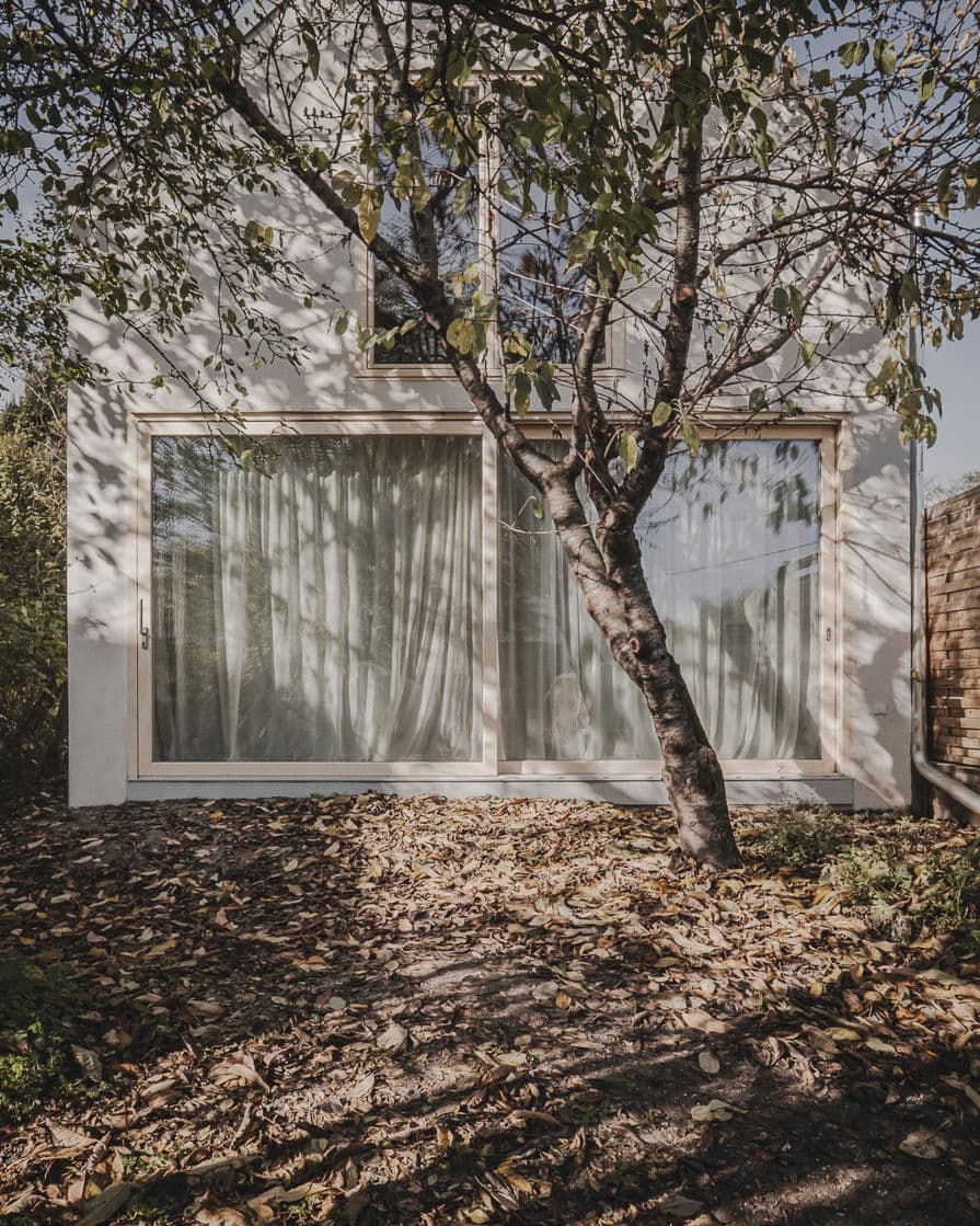 Architectural project - light wood accents, house facade, indoor-outdoor living, private space, home exterior, plaster exterior, tranquil home, soft curtains, tree shadow, natural light, natural tones, eco design, green building, outdoor area, sustainable architecture, neutral tones, daylight, light wood, minimalist design, glass doors, Scandinavian vibe, biophilic design, passive house, white facade, energy efficient design, white, eco friendly home, Nordic style, residential design, relaxing space, exterior view, garden view, residential architecture, garden landscape, textured walls, serene setting, cozy exterior, modern home, contemporary house, calm atmosphere, sliding doors, private garden, natural surroundings, sustainable living, connection to nature, residential facade, urban retreat