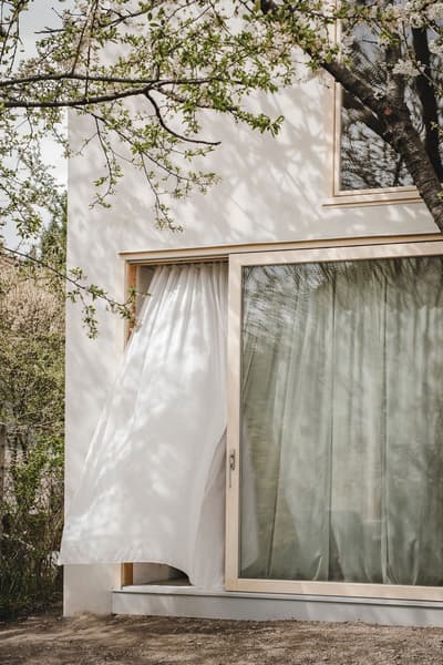 Architectural project - beige accents, bright facade, plaster exterior, tree shadow, outdoor scene, serene vibe, calming atmosphere, eco-friendly design, timber, wooden frame, natural light, warm tones, contemporary architecture, sustainable architecture, beige, minimalist facade, light wood, airy design, urban oasis, simple design, Scandinavian style, neutral palette, minimalist design, tranquil setting, eco home, clean lines, white facade, indoor outdoor, white, large window, energy efficient, plaster, inviting space, garden view, nature integration, modern home, glass door, nordic influence, seamless transition, comfortable living, white exterior, sliding door, floor to ceiling, connection to nature, relaxing home, picture window, Japandi style, modern house