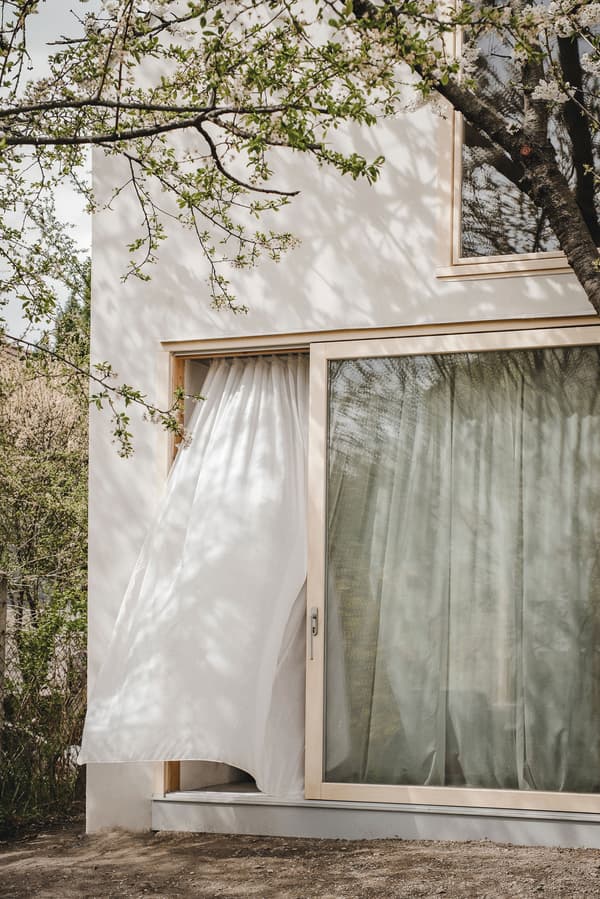 Architectural project - beige accents, bright facade, plaster exterior, tree shadow, outdoor scene, serene vibe, calming atmosphere, eco-friendly design, timber, wooden frame, natural light, warm tones, contemporary architecture, sustainable architecture, beige, minimalist facade, light wood, airy design, urban oasis, simple design, Scandinavian style, neutral palette, minimalist design, tranquil setting, eco home, clean lines, white facade, indoor outdoor, white, large window, energy efficient, plaster, inviting space, garden view, nature integration, modern home, glass door, nordic influence, seamless transition, comfortable living, white exterior, sliding door, floor to ceiling, connection to nature, relaxing home, picture window, Japandi style, modern house
