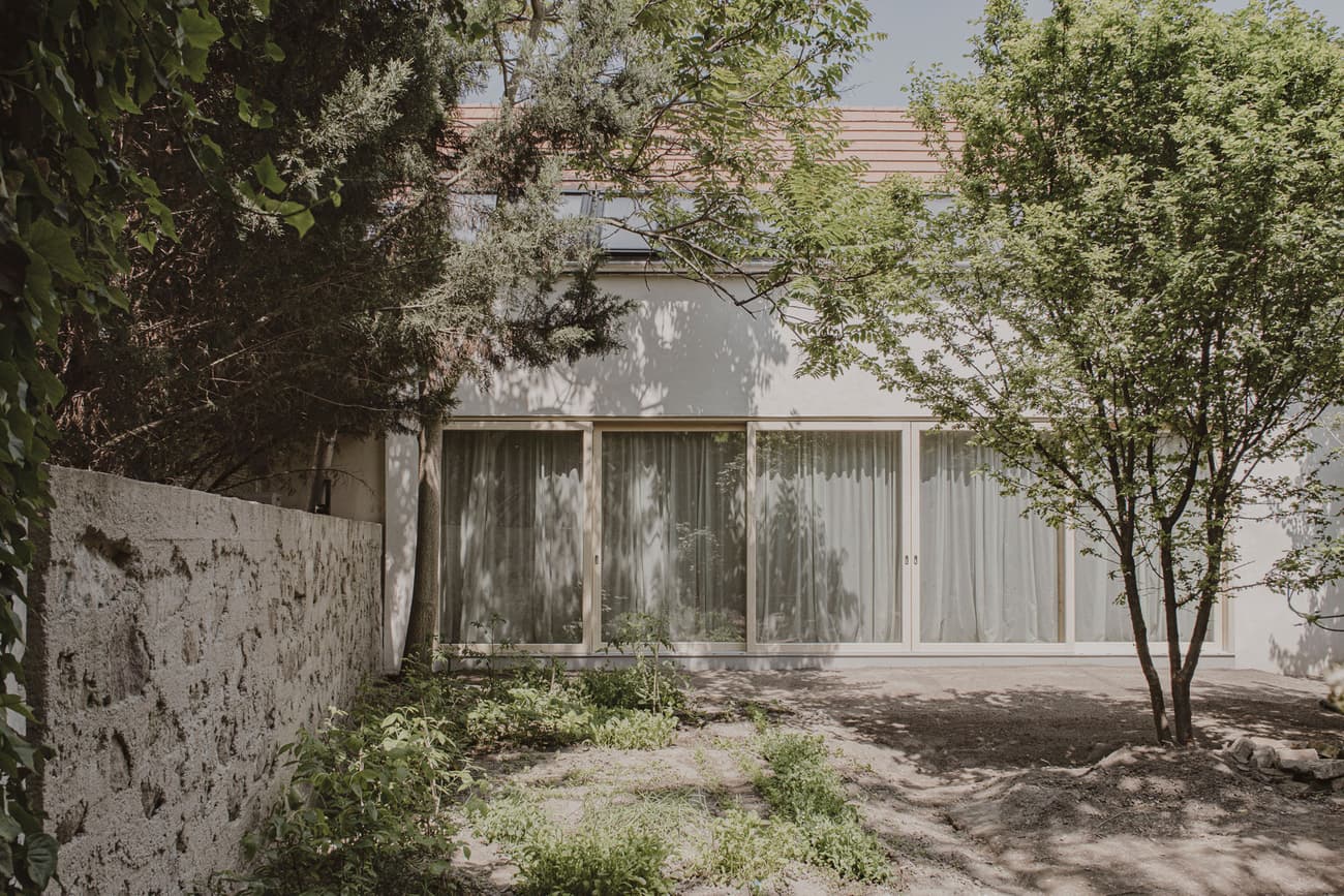 Architectural project - rustic garden, peaceful garden, shaded area, small garden, sustainable garden, modern garden, cozy garden, garden facade, patio doors, minimal design, eco-friendly design, relaxation area, grey tones, outdoor space, natural light, outdoor living, neutral tones, daylight, natural setting, biophilic design, textured wall, earthy tones, nature-inspired, tree canopy, stone wall, family garden, greenery, sunny day, garden view, sliding doors, home garden, private garden, green space, outdoor relaxation, residential facade, modern residential