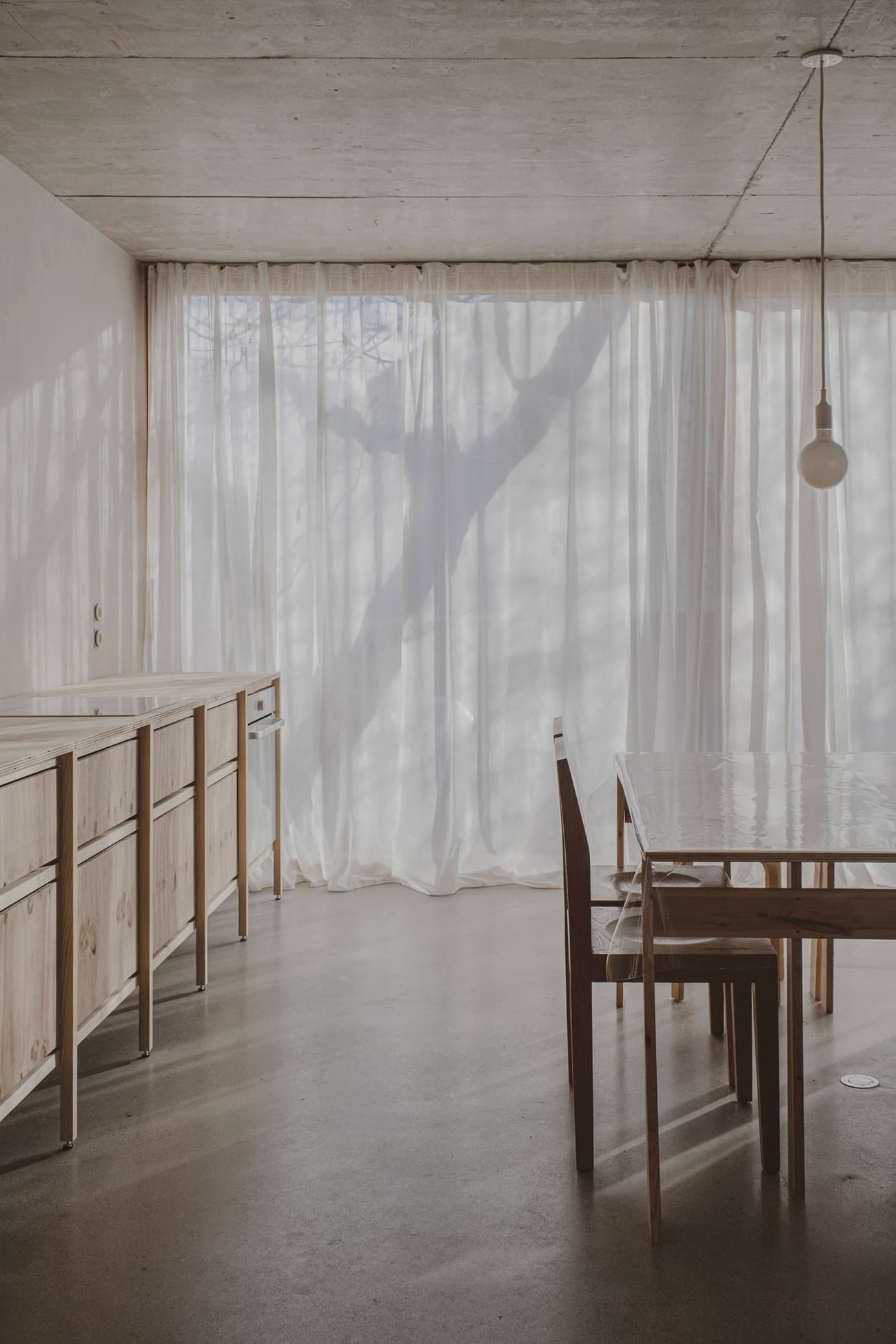 Architectural project - warm neutral, airy interior, modern dining, home dining, cozy dining, wood furniture, polished concrete, elegant simplicity, simple table, sheer curtains, soft shadows, minimalist dining, wooden chair, timber furniture, residential dining, indoor space, wood, natural light, sustainable design, warm tones, neutral tones, beige, concrete, light wood, eco friendly, honey wood, peaceful setting, contemporary design, neutral palette, serene space, relaxed atmosphere, eco home, clean lines, white, textured wall, plaster wall, plaster, open plan, dining area, dining table, minimalist decor, cozy atmosphere, minimalist aesthetic, concrete floor, pendant light, soft light, Japandi style