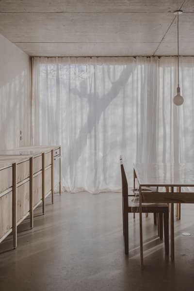 Architectural project - warm neutral, airy interior, modern dining, home dining, cozy dining, wood furniture, polished concrete, elegant simplicity, simple table, sheer curtains, soft shadows, minimalist dining, wooden chair, timber furniture, residential dining, indoor space, wood, natural light, sustainable design, warm tones, neutral tones, beige, concrete, light wood, eco friendly, honey wood, peaceful setting, contemporary design, neutral palette, serene space, relaxed atmosphere, eco home, clean lines, white, textured wall, plaster wall, plaster, open plan, dining area, dining table, minimalist decor, cozy atmosphere, minimalist aesthetic, concrete floor, pendant light, soft light, Japandi style