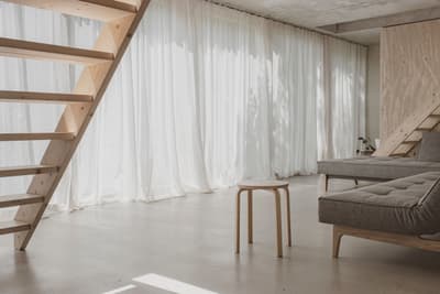 Architectural project - wood wall, hygge vibe, indoor light, modern loft, loft space, polished concrete, floor-to-ceiling curtains, sheer curtains, light palette, inviting ambiance, modular sofa, cozy interior, wood, timber, natural light, warm tones, eco design, grey, neutral tones, daylight, beige, concrete, light wood, simple design, natural textures, Scandinavian style, warm wood, contemporary home, clean lines, large windows, white, Nordic style, beige tones, airy space, open layout, open plan, living area, sustainable material, calm atmosphere, residential, concrete floor, home interior, timber wall, relaxed space, soft light, modern interior, wooden stool