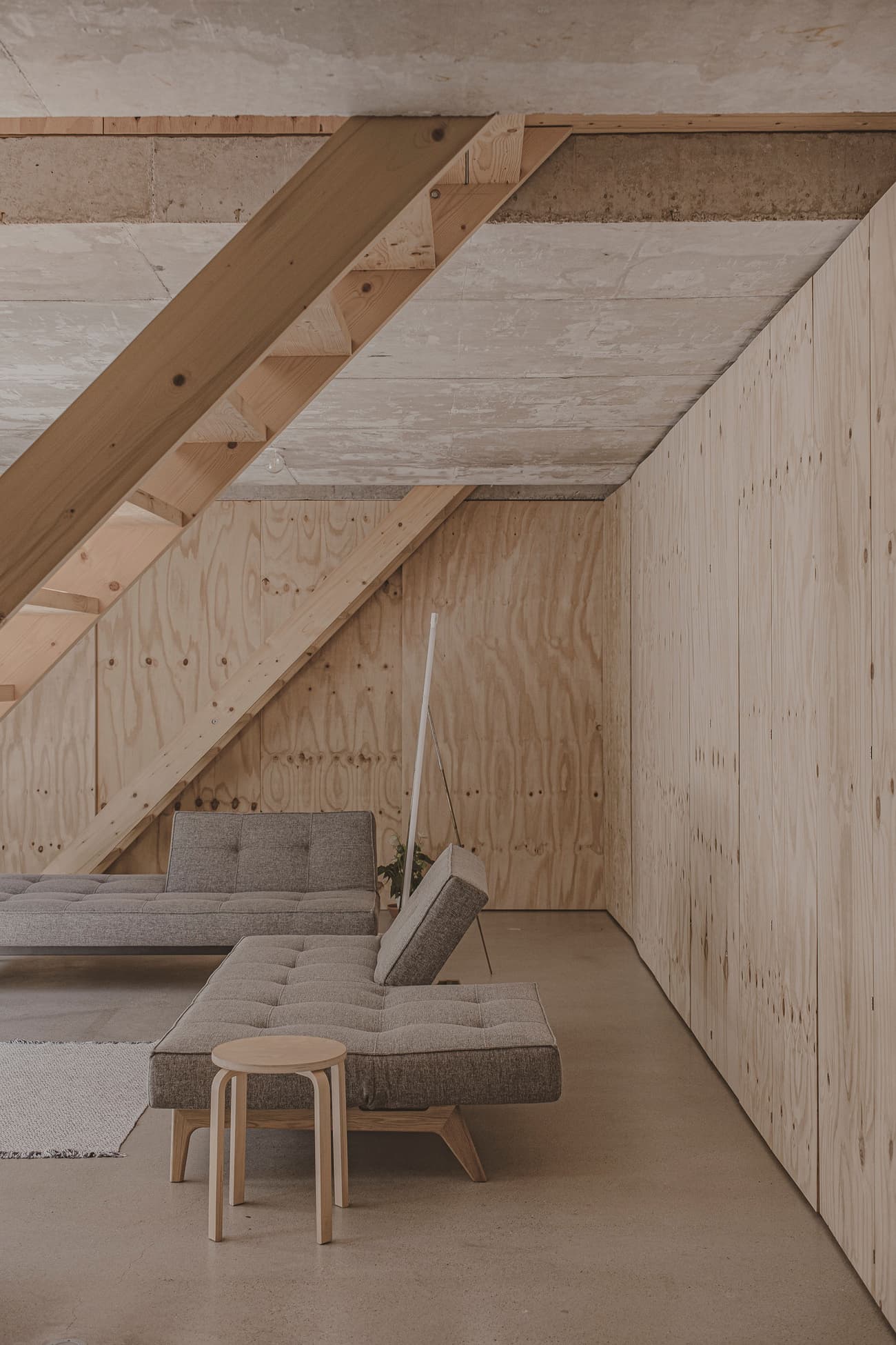 Architectural project - lounging area, light grey, industrial loft, plywood walls, angular design, concrete ceiling, modern loft, geometric elements, studio apartment, city apartment, modular sofa, modular furniture, cozy loft, natural materials, sustainable materials, timber, grey tones, raw materials, natural light, exposed structure, contemporary style, daylight, plywood, beige, concrete, light wood, natural wood, simple design, Scandinavian style, neutral palette, minimalist design, casual seating, modern aesthetics, plywood panels, timber walls, clean lines, architectural details, small space, compact design, open layout, open plan, inviting space, earthy tones, warm atmosphere, relaxing space, cozy corner, nordic influence, soft tones, wood textures, eco conscious design, minimalist interior, urban living