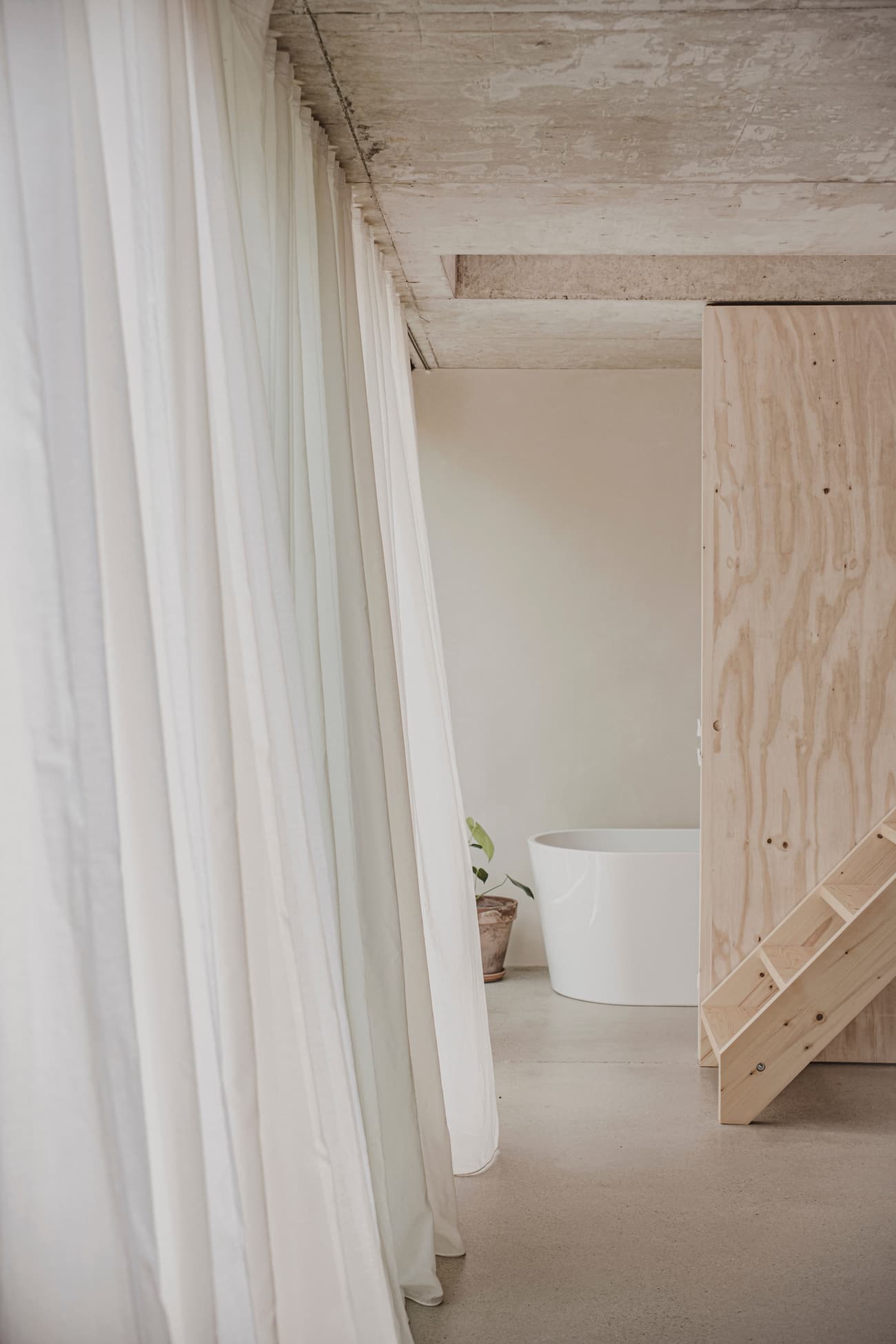Architectural project - exposed concrete, concrete ceiling, raw interior, freestanding tub, bathtub, relaxation space, wellness space, soft lighting, serene environment, eco-friendly design, wood, natural light, warm tones, contemporary style, neutral tones, plywood, beige, concrete, light wood, Scandinavian influence, compact space, natural textures, neutral palette, minimalist design, plywood wall, wood panels, white, open layout, modern home, calm atmosphere, earthy textures, soft tones, interior space, spa-like, understated elegance, Japandi style