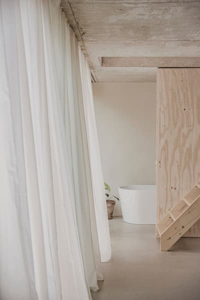 Architectural project - exposed concrete, concrete ceiling, raw interior, freestanding tub, bathtub, relaxation space, wellness space, soft lighting, serene environment, eco-friendly design, wood, natural light, warm tones, contemporary style, neutral tones, plywood, beige, concrete, light wood, Scandinavian influence, compact space, natural textures, neutral palette, minimalist design, plywood wall, wood panels, white, open layout, modern home, calm atmosphere, earthy textures, soft tones, interior space, spa-like, understated elegance, Japandi style