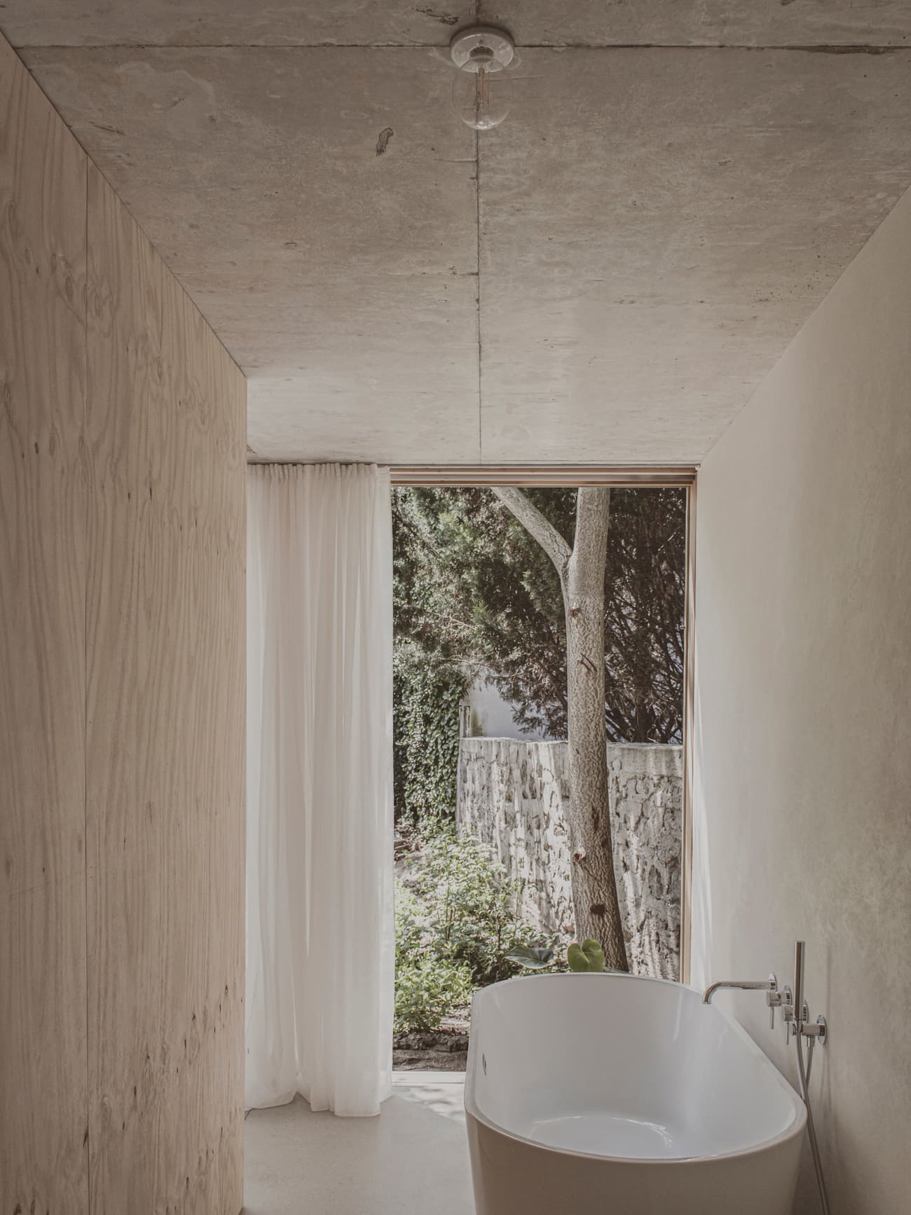 Architectural project - wood wall, unfinished look, concrete ceiling, curtain, bathroom, minimalist bathroom, contemporary bathroom, spa-like bathroom, freestanding tub, bathtub, intimate space, natural materials, tranquil space, wood, timber, natural light, privacy screen, sustainable design, glass, grey, neutral tones, daylight, beige, concrete, light wood, low carbon design, eco friendly, organic design, serene atmosphere, Scandinavian style, minimalist design, soft textures, light tones, plywood wall, earth tones, nature view, indoor outdoor, white, large window, airy space, cozy corner, garden view, raw finish, bright interior, modern bathroom, picture window, Japandi style, modern retreat