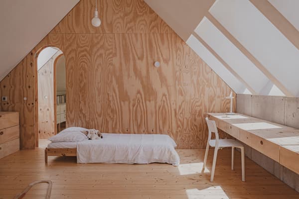 Architectural project - minimalist home, plywood walls, airy room, attic bedroom, white bedding, simple bed, built-in desk, minimalist desk, space optimization, warm interior, eco-friendly design, sustainable materials, timber, relaxed vibe, natural light, daylight, plywood, light wood, natural wood, modern aesthetic, Scandinavian influence, honey wood, modern simplicity, cozy retreat, neutral palette, serene space, timber walls, wood floor, timber elements, Nordic design, beige tones, small space, compact design, inviting space, wood texture, wooden flooring, peaceful vibe, bright interior, calm atmosphere, cozy home, sustainable living, minimalist bedroom, sloped ceiling, skylight, vaulted ceiling