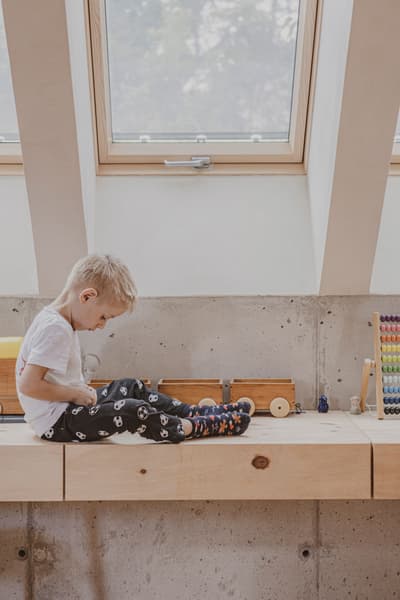 Architectural project - casual vibe, indoor setting, wooden toys, window seating, simple interior, minimal design, natural materials, wood, timber, natural light, sustainable design, warm tones, daylight, beige, concrete, light wood, compact space, minimalist style, relaxed atmosphere, Scandinavian vibe, eco-friendly materials, light tones, warm wood, white, Nordic design, small space, cozy nook, family home, modern home, home design, interior space, playful space, concrete wall, skylight, home renovation, residential interior, creative corner