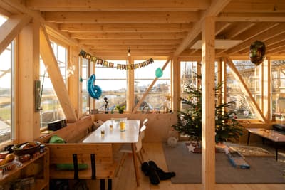 Architectural project - warm interior, natural materials, wood, timber, natural light, sustainable design, glass, warm tones, eco design, exposed beams, daylight, beige, brown, light wood, wooden beams, rustic modern, Scandinavian style, wooden floor, casual seating, structural beams, modern rustic, nature view, large windows, Nordic design, eco friendly home, cozy vibe, wooden interior, wood texture, relaxed living, wood cabin, timber cabin, rustic cabin, cozy cabin, timber interior, open layout, open plan, family space, living area, dining area, wooden table, dining table, white chairs, indoor trees, holiday decor, festive atmosphere, glass walls, panoramic view, inviting space, hygge style, minimalist decor, holiday, program space, social gathering, green home