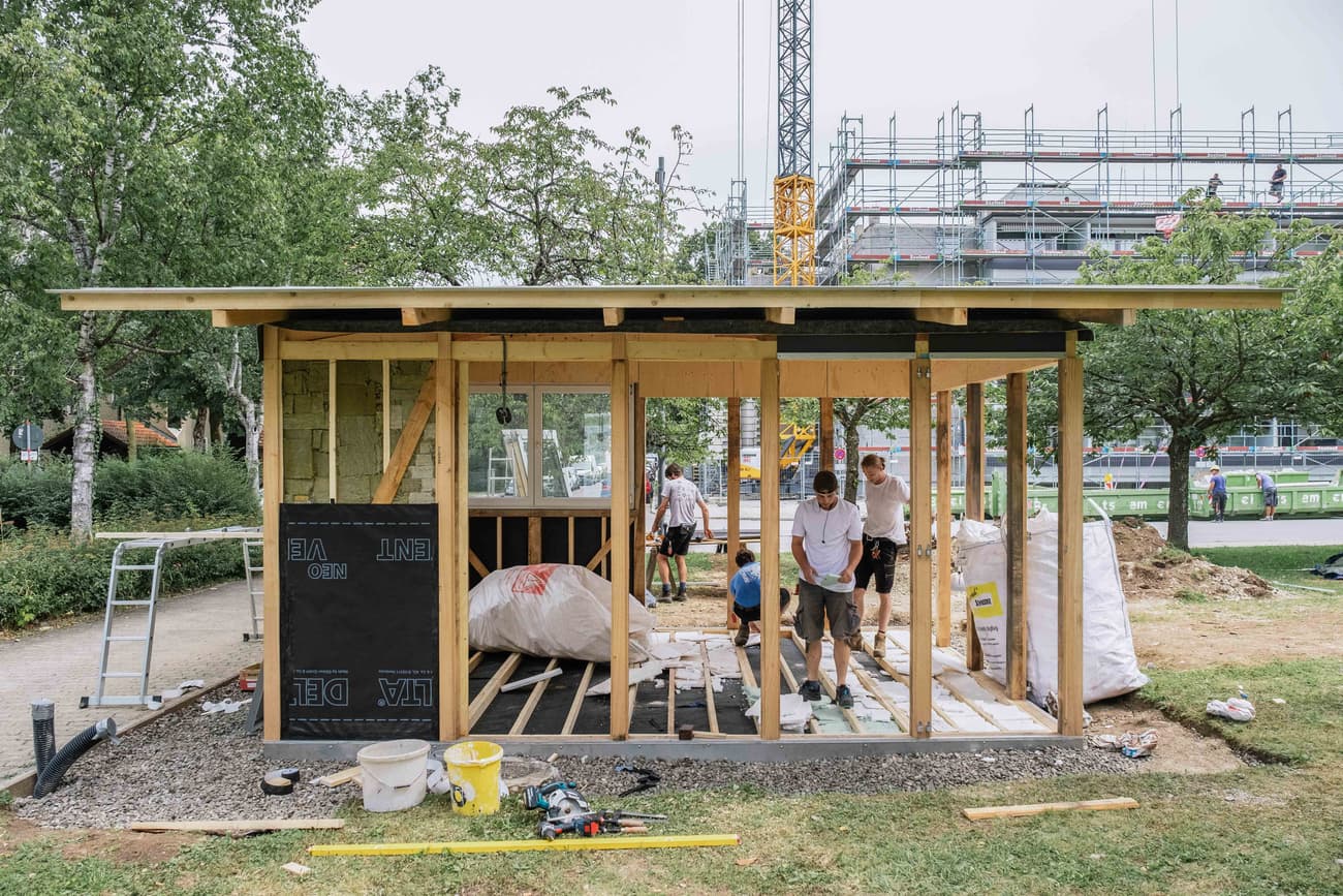 Architectural project - construction zone, collaborative work, new build, natural materials, wood, timber, temporary structure, scaffolding, urban setting, raw materials, outdoor space, timber frame, passive design, glass, natural tones, modular design, green building, innovative design, lightweight construction, sustainable architecture, construction site, construction workers, building assembly, outdoor construction, teamwork, urban development, building site, beige, timber facade, light wood, timber construction, prefab building, open framework, construction details, building process, wood structure, sustainable building, eco construction, timber walls, natural texture, eco-friendly building, green design, wooden facade, structural elements, architectural process, community project