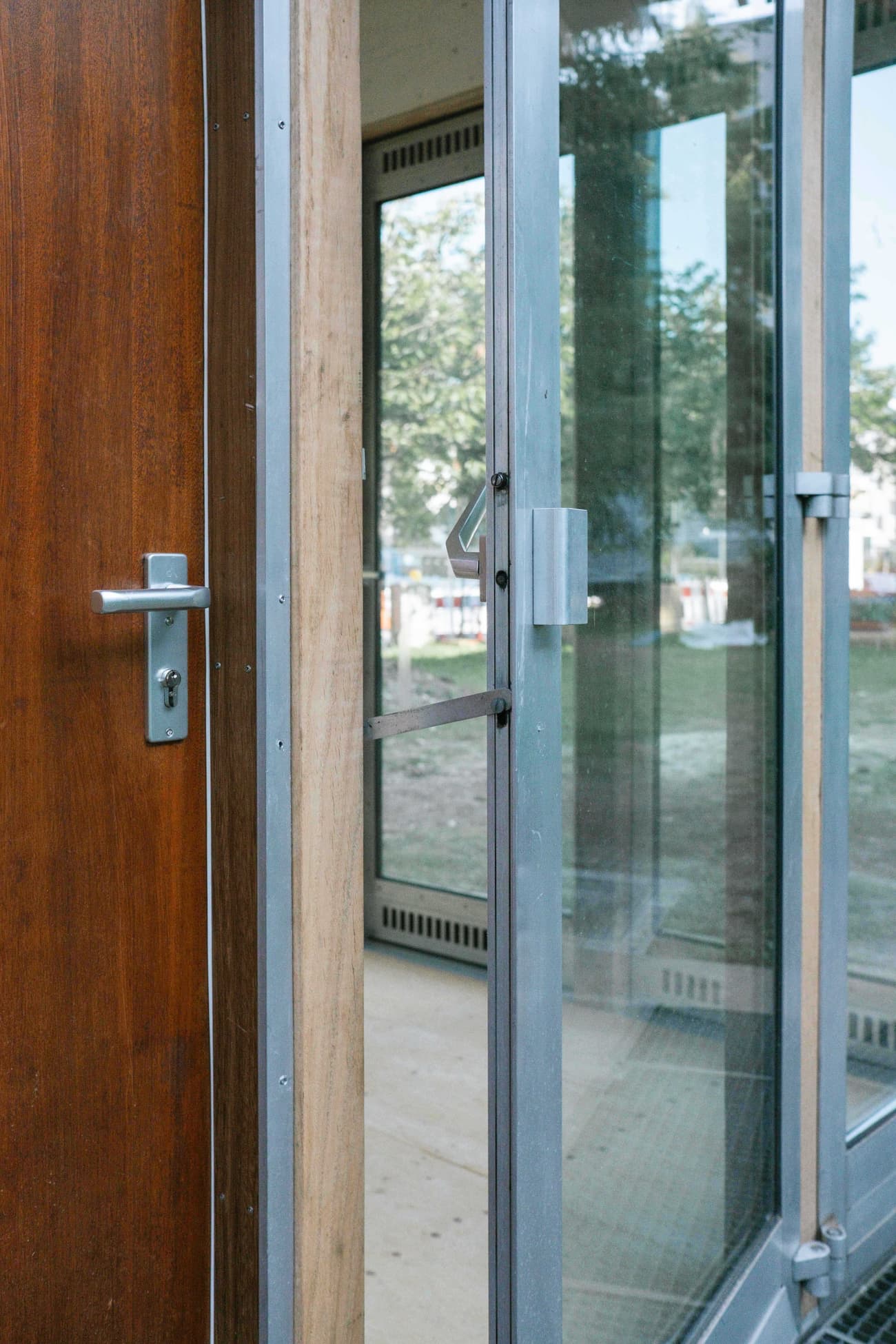Architectural project - silver accents, metalwork, modern entrance, streamlined design, glass panel, architectural detail, natural light, contemporary style, city architecture, functional design, minimalist design, neutral colors, steel frame, warm wood, durable materials, outdoor view, wood frame, sleek design, glass door, urban architecture, wooden door, metal handle, urban facade, modern materials, clear glass