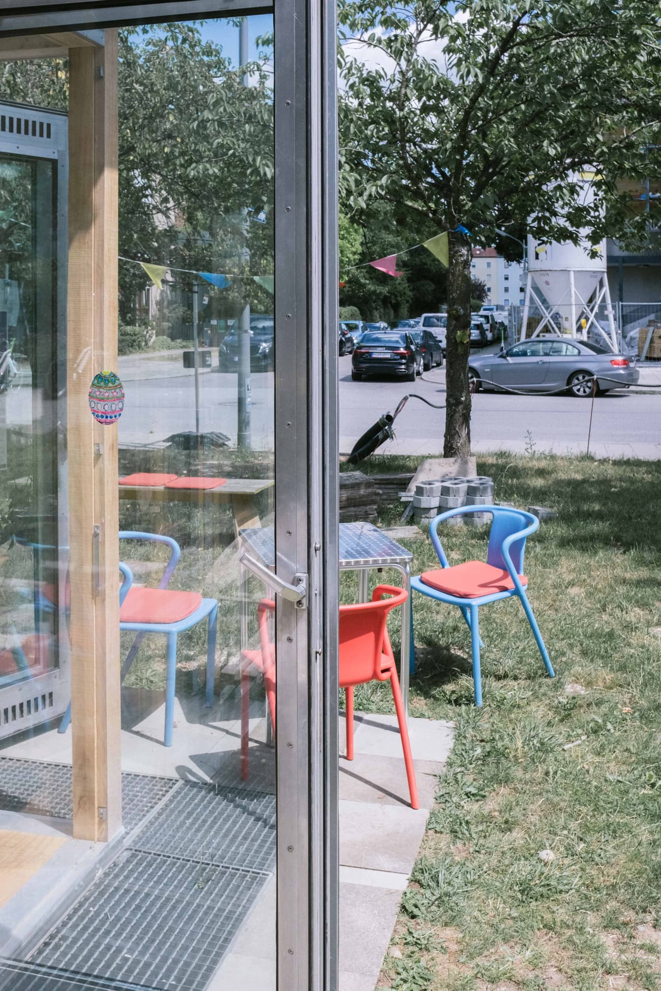 Architectural project - city garden, sliding glass, garden chairs, colorful chairs, patio chairs, timber details, playful seating, blue chairs, urban setting, metal frame, playful design, outdoor space, timber frame, natural light, outdoor living, sustainable design, functional space, daylight, light wood, eco friendly, contemporary design, minimalist style, casual seating, outdoor seating, vibrant colors, bright colors, indoor outdoor, alfresco dining, garden view, summer vibe, open air, glass door, garden seating, green lawn, modern exterior, urban garden, metal handle