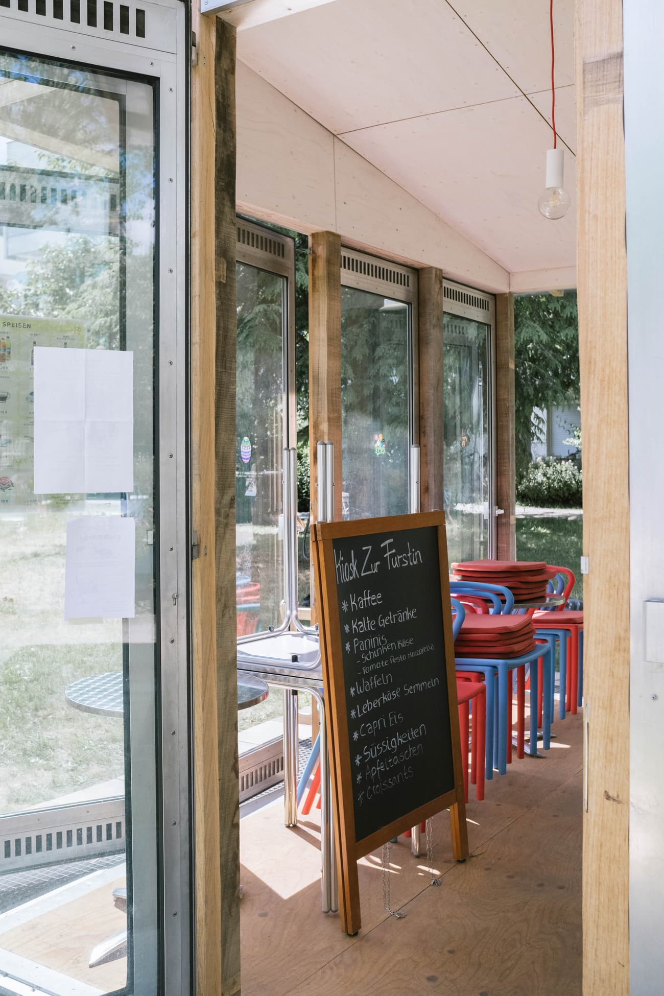 Architectural project - cozy feel, transparent facade, welcoming vibe, street cafe, blue chairs, simple interior, intimate space, eco-friendly design, wood, natural light, glass, natural tones, exposed structure, functional space, daylight, light wood, blue, Scandinavian influence, minimalist design, eco materials, outdoor cafe, relaxed atmosphere, pop-up cafe, informal setting, sustainable structure, exposed wood, modern rustic, nature view, light filled, indoor outdoor, compact design, timber interior, glass walls, social gathering, casual dining, bright space, open view, urban retreat, wood interior, red