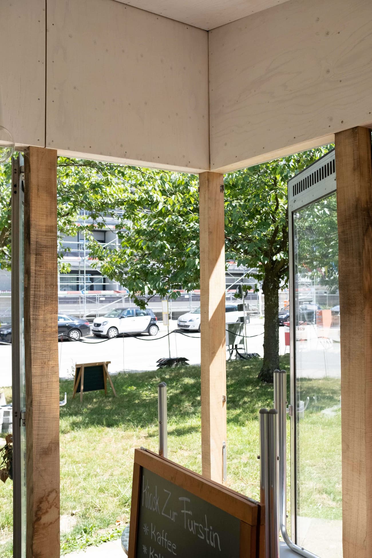 Architectural project - urban greenery, exposed timber, glazed facade, casual vibe, urban cafe, transparent facade, gathering spot, transparent, open entrance, natural materials, wood, timber, urban setting, cityscape, wooden frame, natural light, sustainable design, glass, eco design, community space, green, timber structure, daylight, light wood, eco friendly, natural setting, sunlight, rustic charm, light brown, minimalist design, relaxed atmosphere, outdoor seating, glass doors, raw wood, earth tones, biophilic design, indoor outdoor, outdoor view, inviting entrance, nature integration, open air, bright space, green surroundings, airy feel, wood paneling, street view