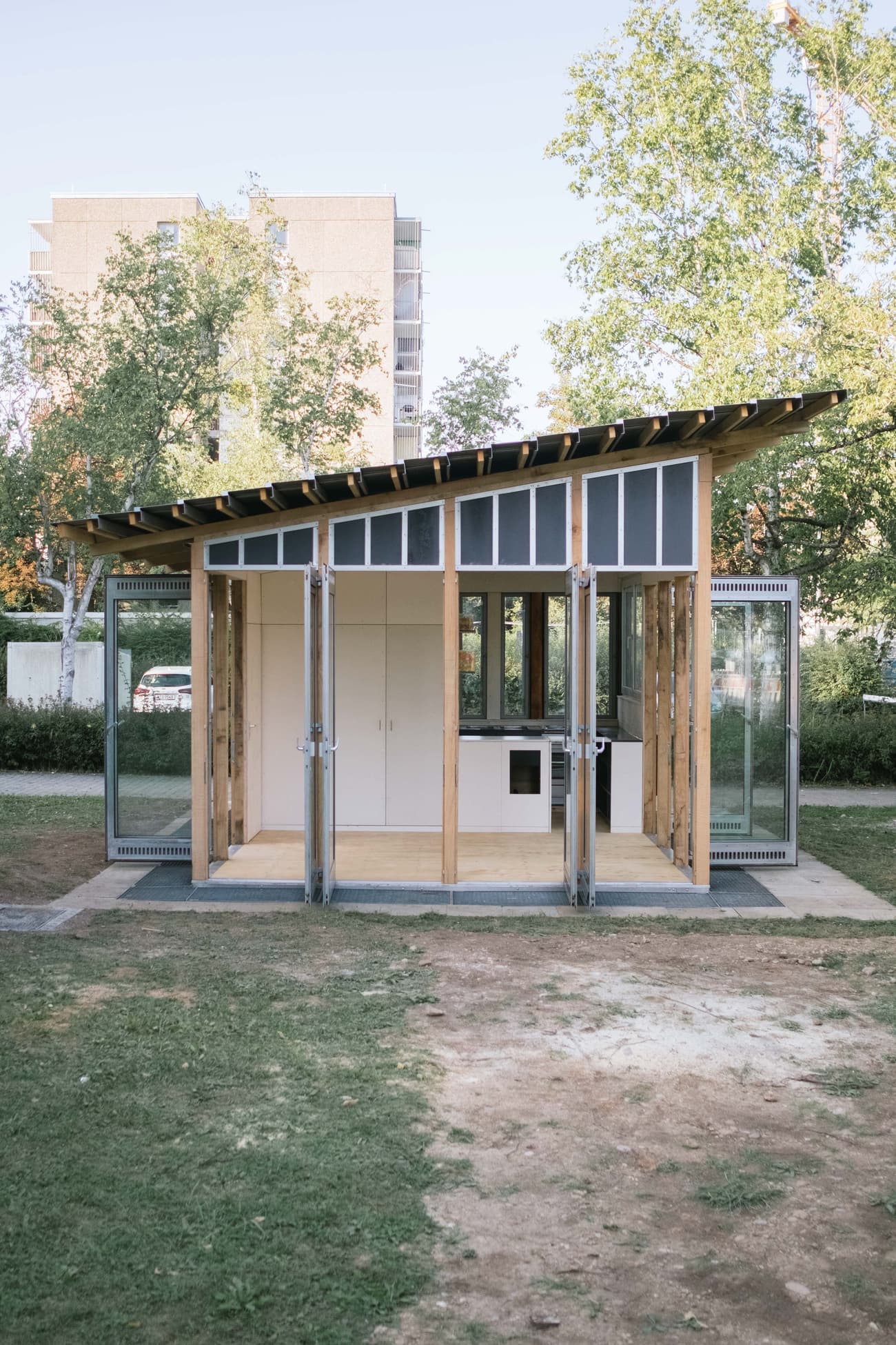 Architectural project - tiny house, flexible space, minimal living, wooden siding, wood, timber, temporary structure, metal, timber frame, natural light, sustainable design, glass, warm tones, modular design, green building, transparent walls, grey, neutral tones, daylight, beige, light wood, eco friendly, natural setting, retreat space, open facade, wood structure, biophilic design, passive house, indoor outdoor, timber cladding, outdoor view, open plan, nature connection, garden retreat, minimalist space, compact living, glass facade, small home